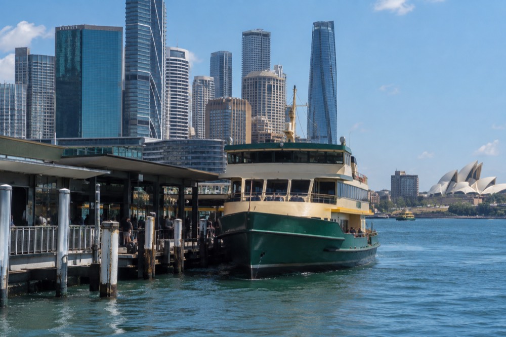 A ferry wharf at Circular Quay with a Sydney ferry at the berth and the city skyline behind it