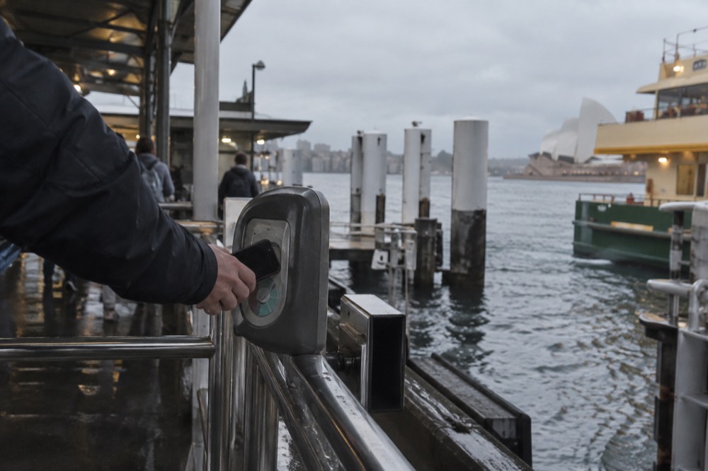 A hand tapping a phone on a ferry card reader at a Sydney wharf
