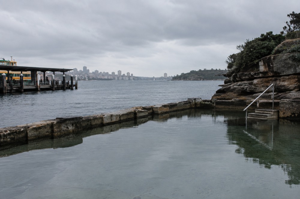 A rock-walled ocean pool beside the coastline with still water reflecting a winter sky