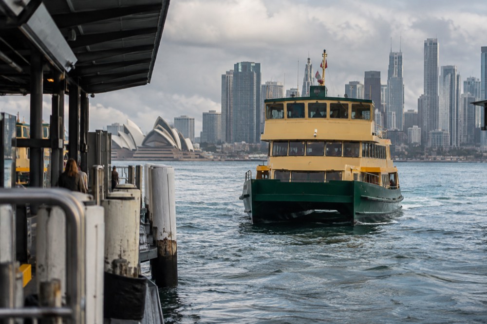 A Sydney ferry approaching a wharf with the harbour skyline behind it