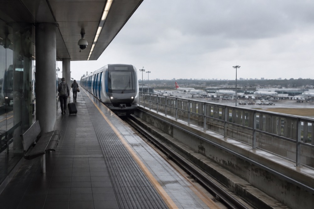 A train on an elevated airport railway station platform beside a terminal building in Sydney