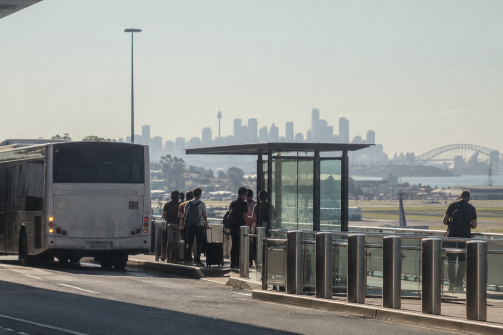 A bus stop outside a Sydney airport terminal with a city skyline in the distance