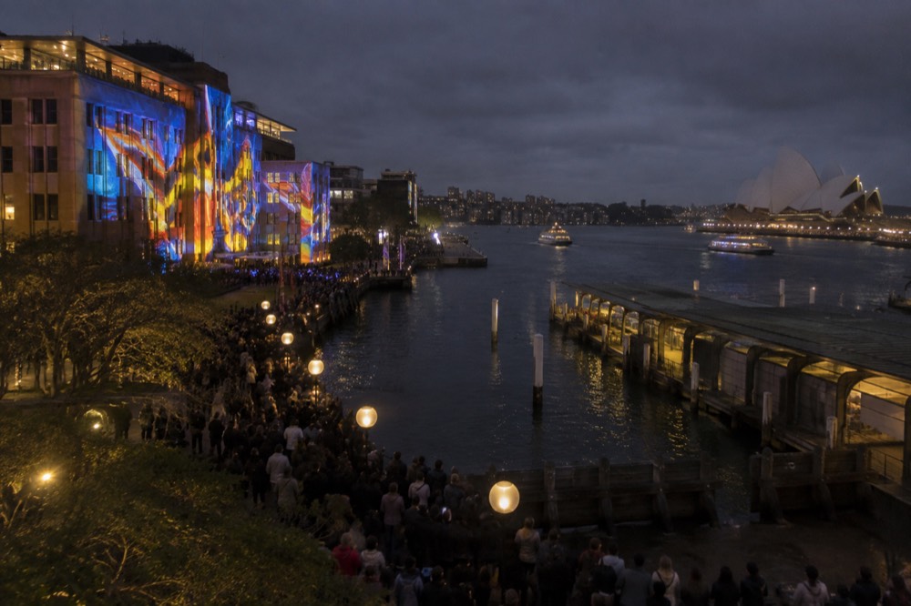 Crowds watching a light installation projected onto a building during a night festival