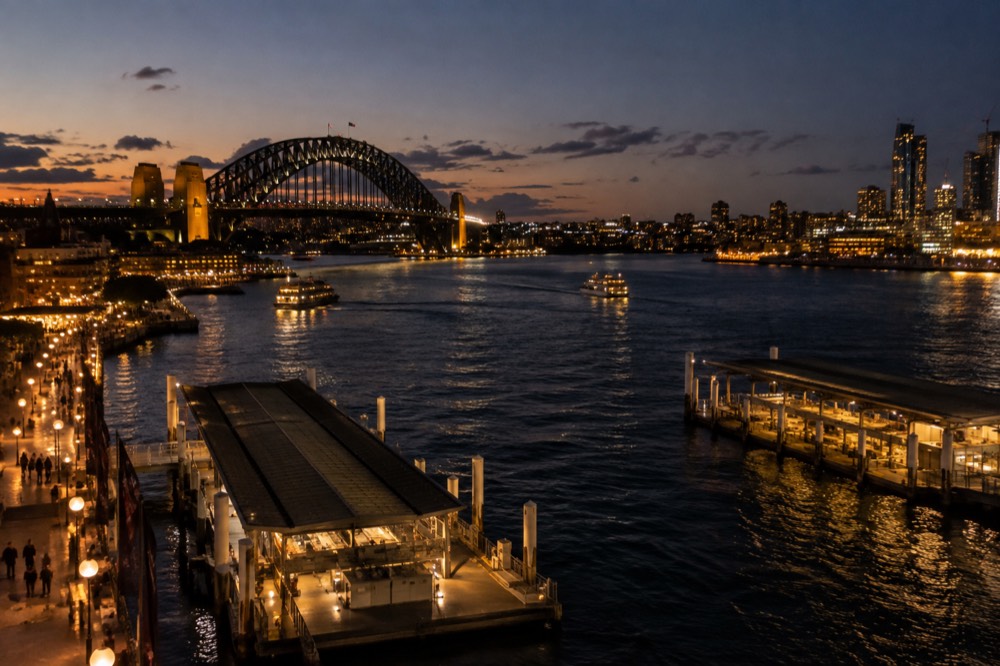 The top of the bridge arch at dusk with the illuminated city skyline stretching to the horizon