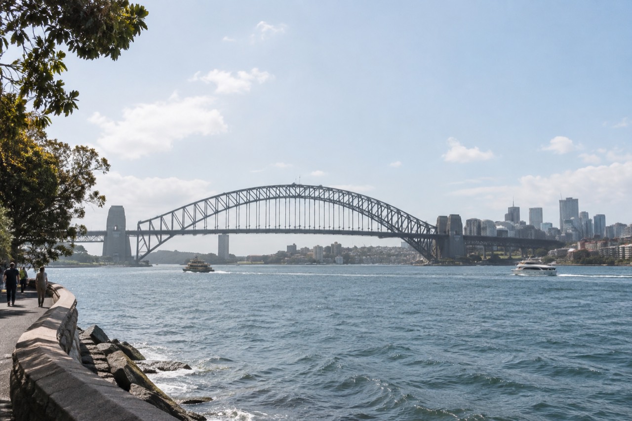 The steel arch of Sydney Harbour Bridge rising above the water with the city skyline behind it