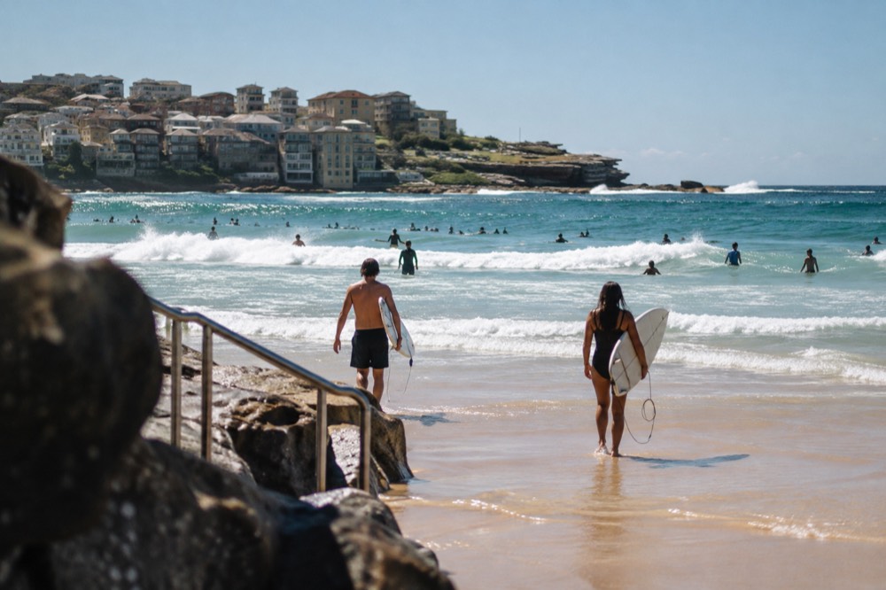 Golden sand at Bondi Beach with surfers walking toward the water and waves breaking
