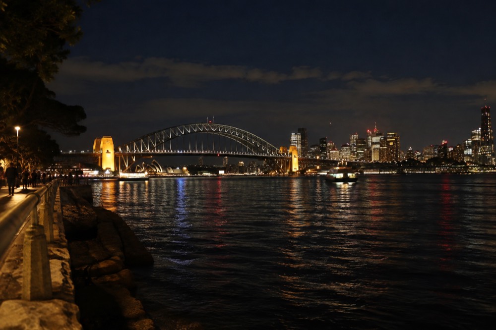 The Sydney Harbour Bridge arch at night with the illuminated skyline of the city behind it