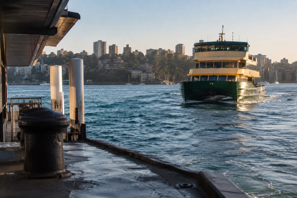 Ferry approaching a wharf on Sydney Harbour with green hillside and city buildings in the background