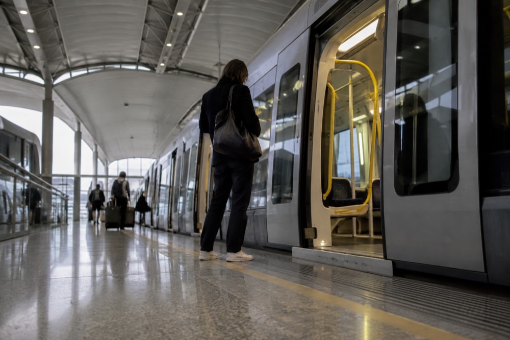 A Sydney airport train at an indoor platform with a passenger waiting near the doors