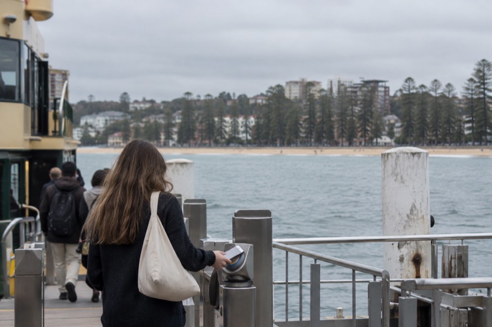 A passenger tapping a phone on an Opal reader at a ferry wharf