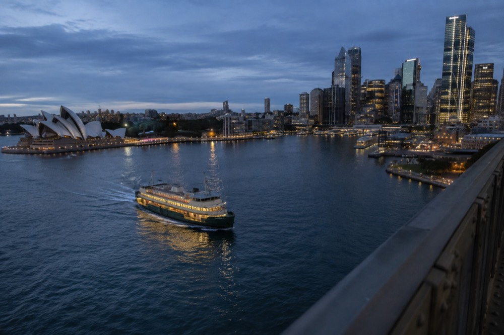 A ferry crossing Sydney Harbour seen from the pedestrian walkway of the Harbour Bridge, with Circular Quay and the city skyline behind it