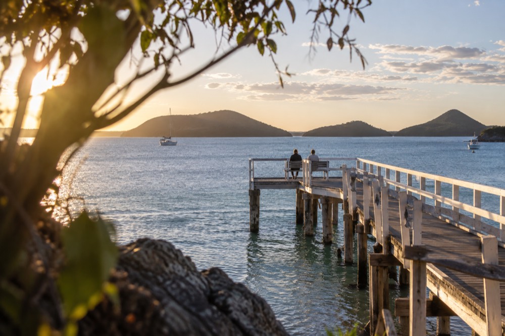 Wooden jetty stretching over calm turquoise bay water toward distant headlands