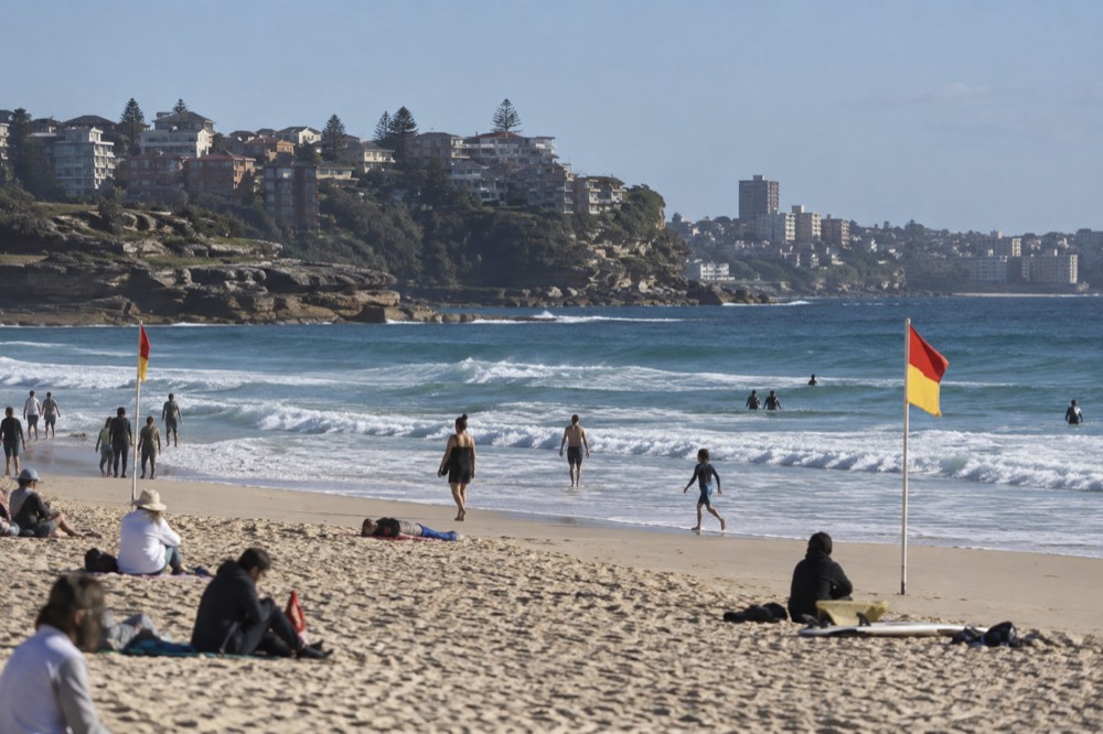 A patrolled Sydney beach with red and yellow flags planted on the sand between the surf