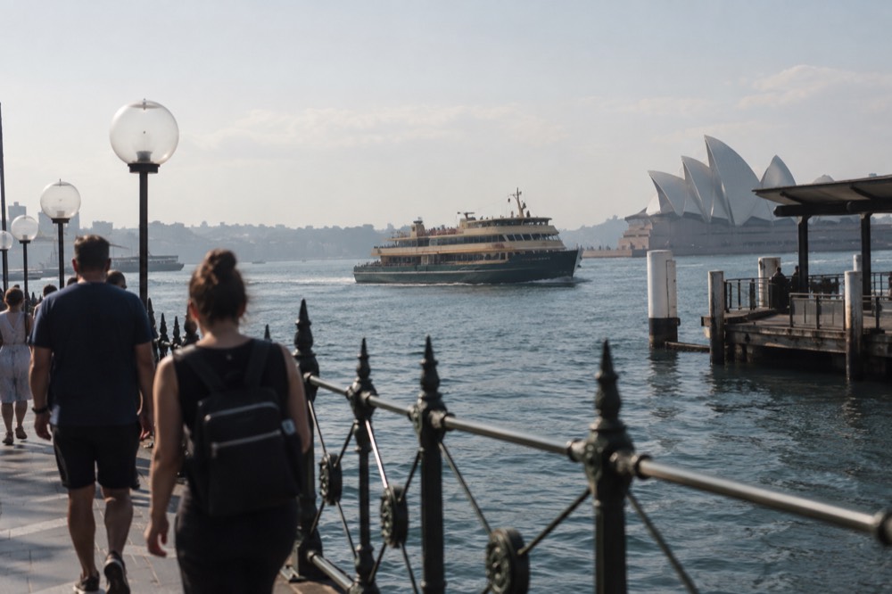 A ferry crossing Sydney Harbour with walkers on the quay in the foreground