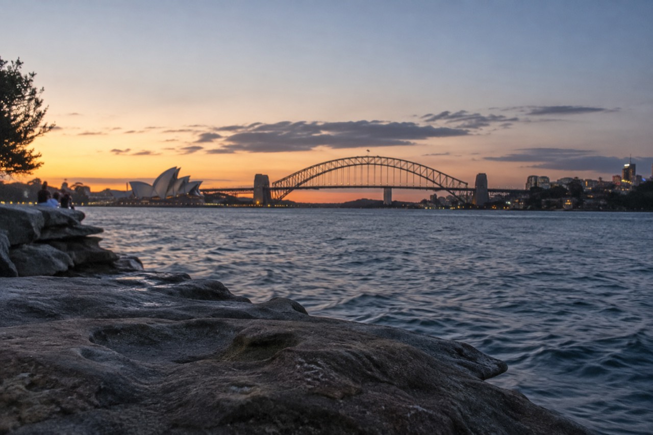 Sydney Harbour with the Opera House and Harbour Bridge seen from a headland at golden hour