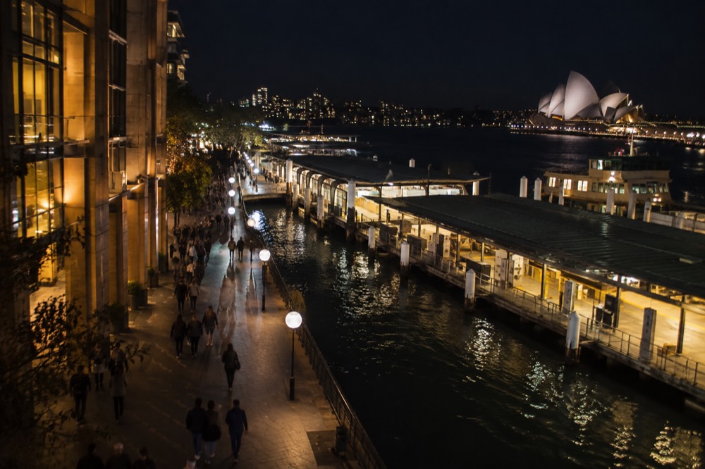 A well-lit Sydney city street at night with pedestrians walking under illuminated buildings