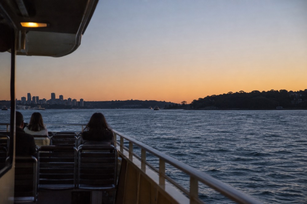 A ferry top deck with harbour headlands and open water ahead under a clear sky
