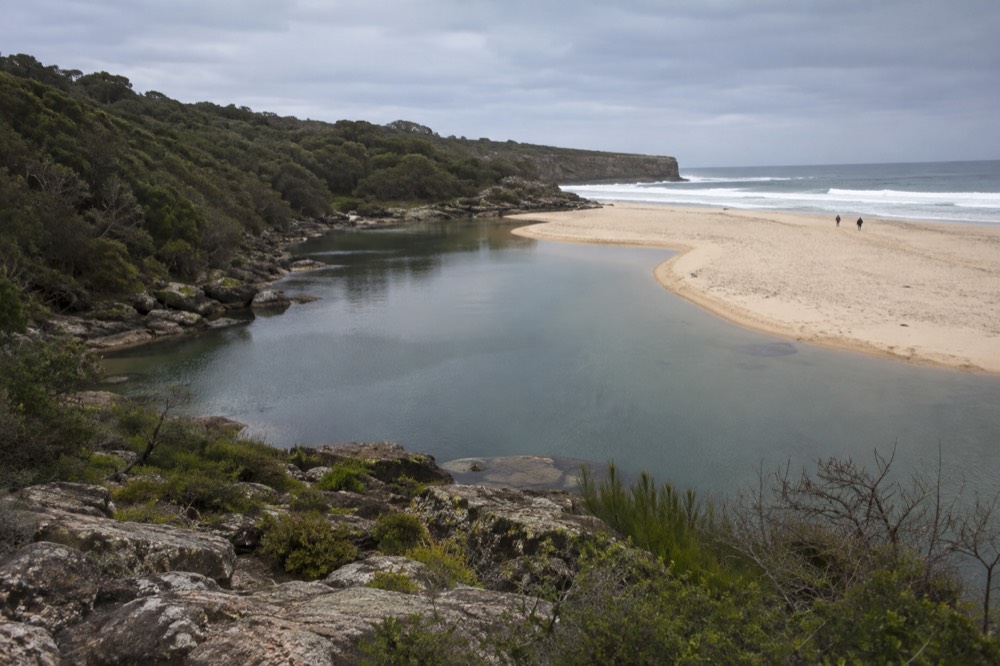 A calm creek lagoon meeting a sandy beach behind a sand spit