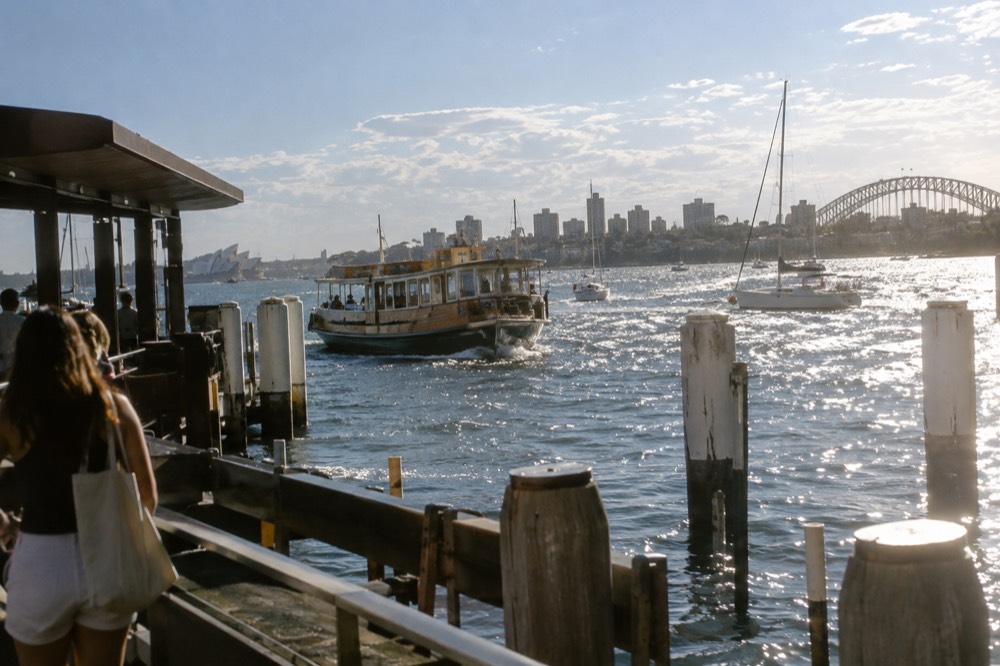 Wooden ferry and sailing boats on sparkling harbour water in the late afternoon light
