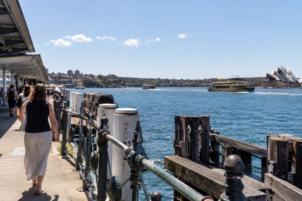 Sandstone headland and calm blue harbour water with ferries crossing in the distance