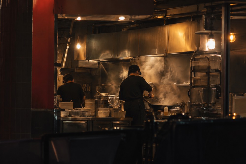 Steam rising from woks in a busy Chinatown kitchen at night