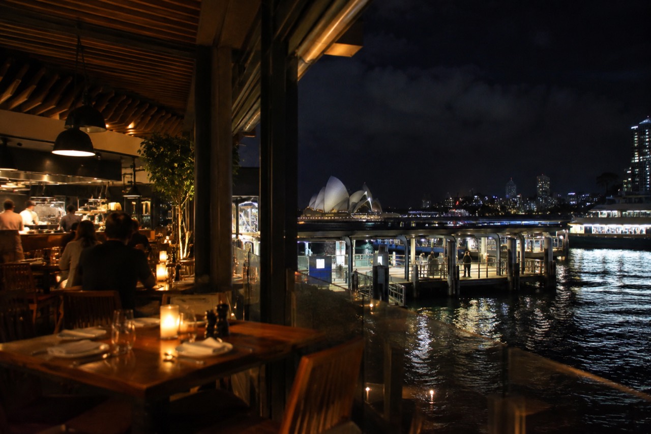 A warmly lit Sydney restaurant interior at night with timber tables and an open kitchen