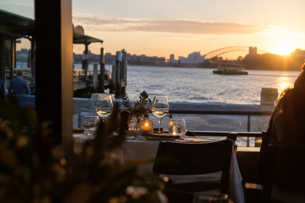 A candlelit fine dining table set with glassware overlooking Sydney Harbour at dusk
