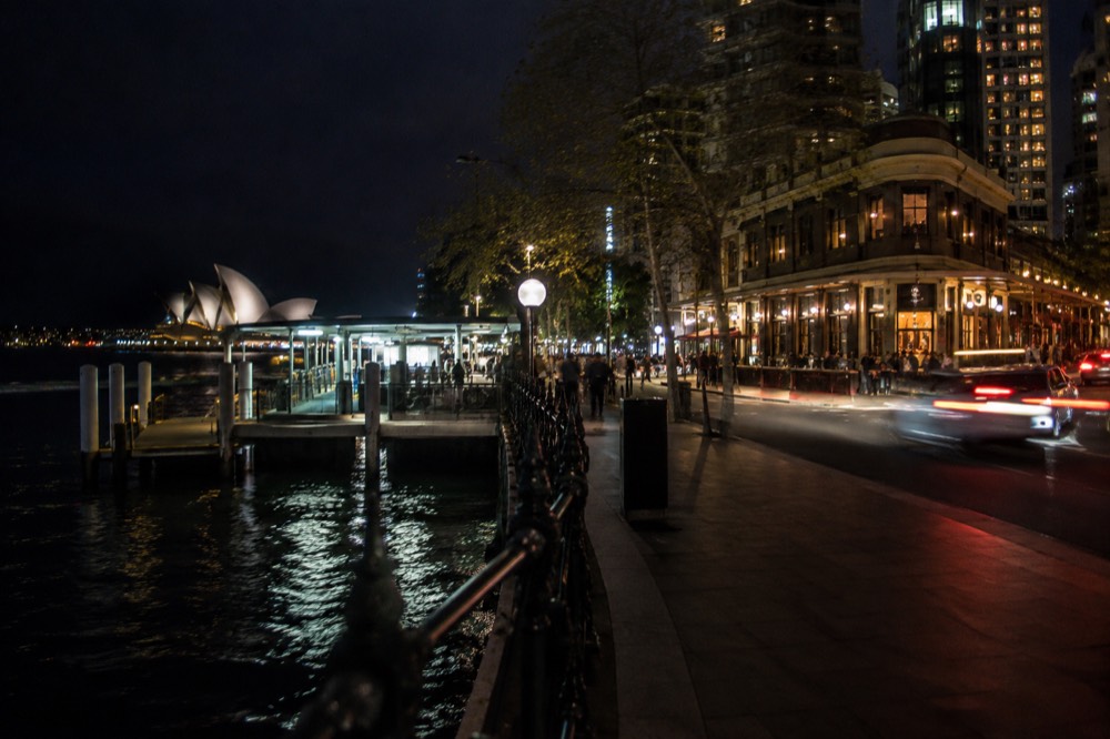 A lit-up corner pub on a Sydney street at night with traffic light trails along the road