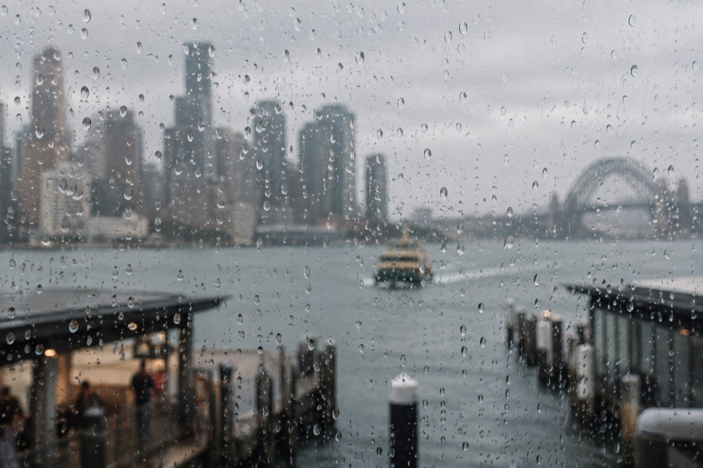 Raindrops on a window with the Sydney skyline and harbour blurred behind the glass