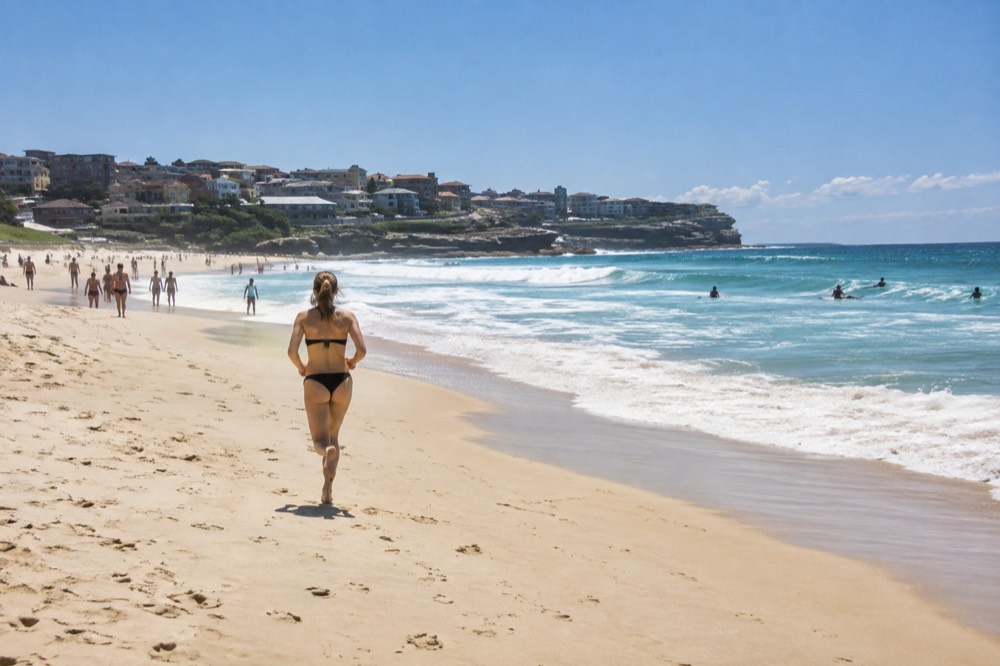 Bondi Beach crescent of sand with surfers in the water and the cliff walk beyond