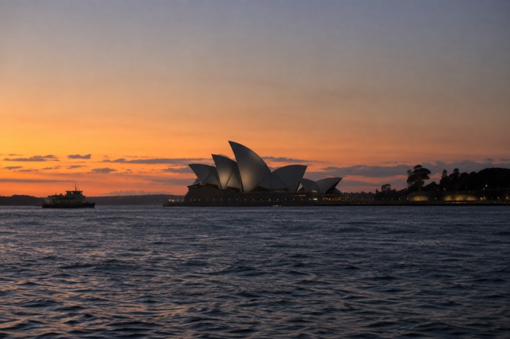 Sydney Opera House white sails seen across dark harbour water at sunset