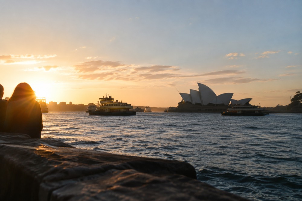 Sydney Opera House sails seen across Circular Quay at dusk with ferries on the harbour
