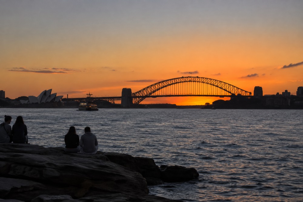 Sydney Harbour at sunset with the Opera House and Harbour Bridge silhouetted against an orange sky