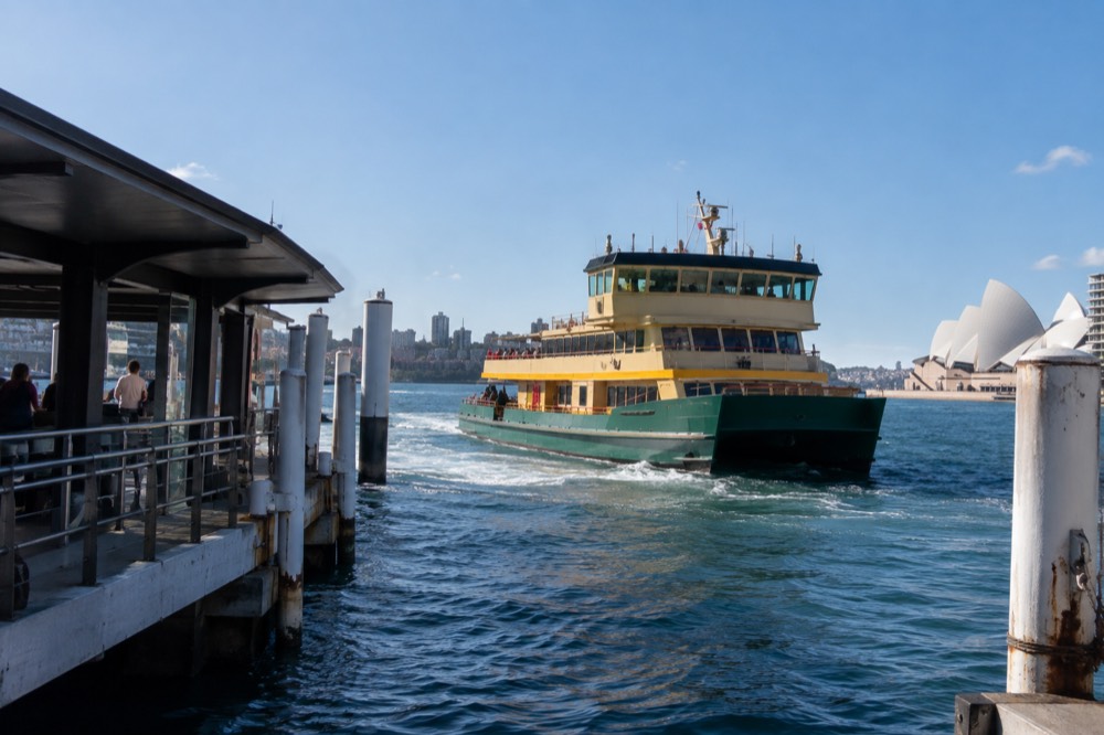 A green and yellow Sydney ferry pulling away from a Circular Quay wharf