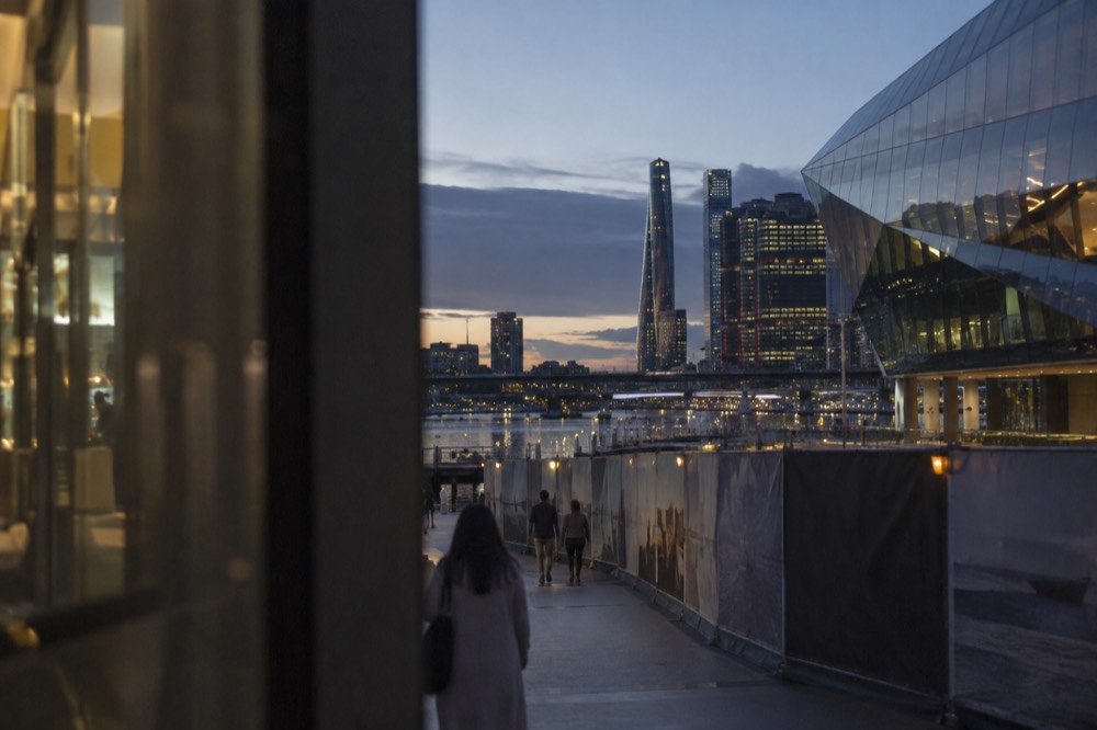 Modern glass museum building beside a harbour walkway with construction hoarding