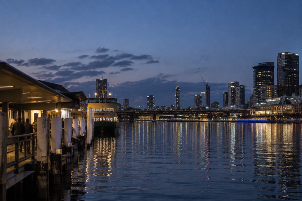 Ferry wharf at dusk with city lights reflecting on calm harbour water