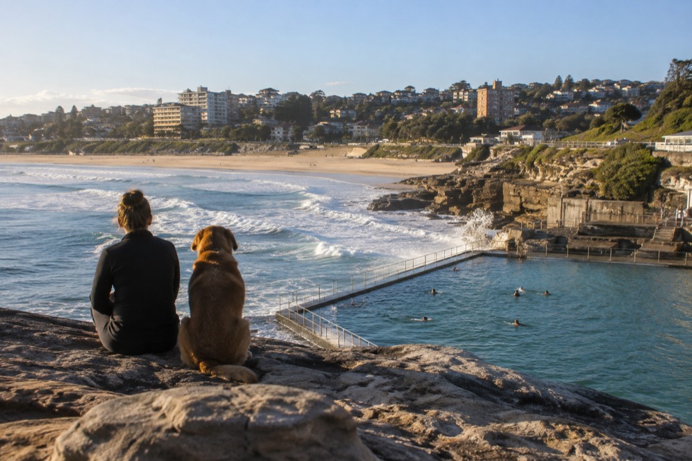 Ocean pool and sandy beach below sandstone cliffs on a clear morning