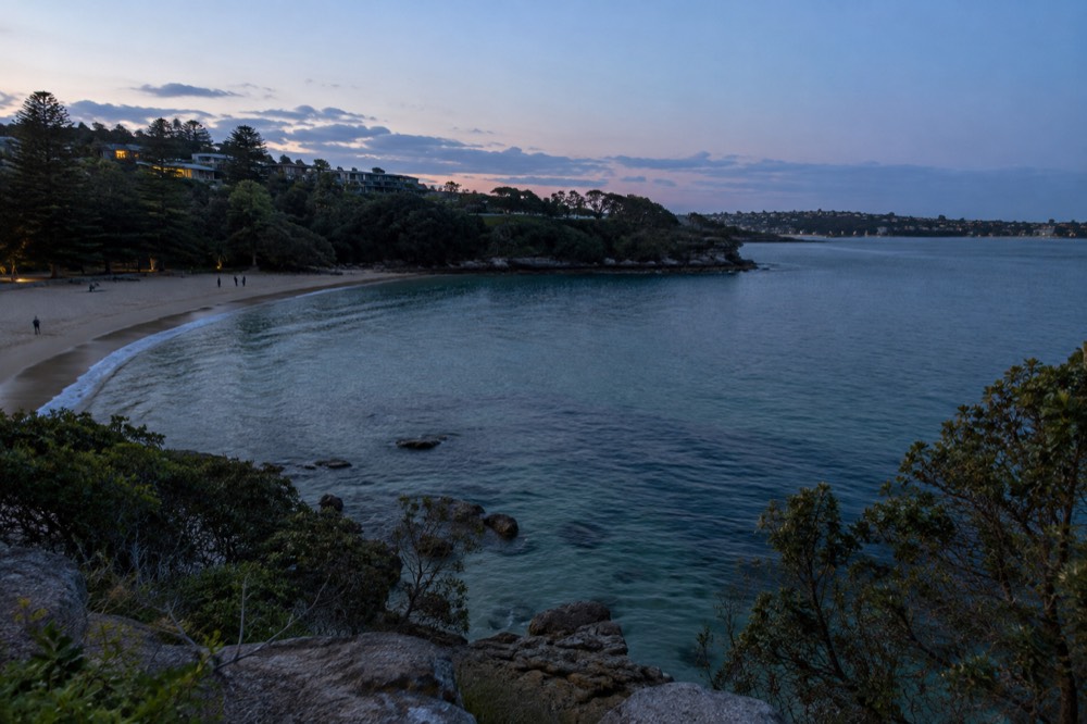 A sheltered sandy cove with clear shallow water and trees along the foreshore