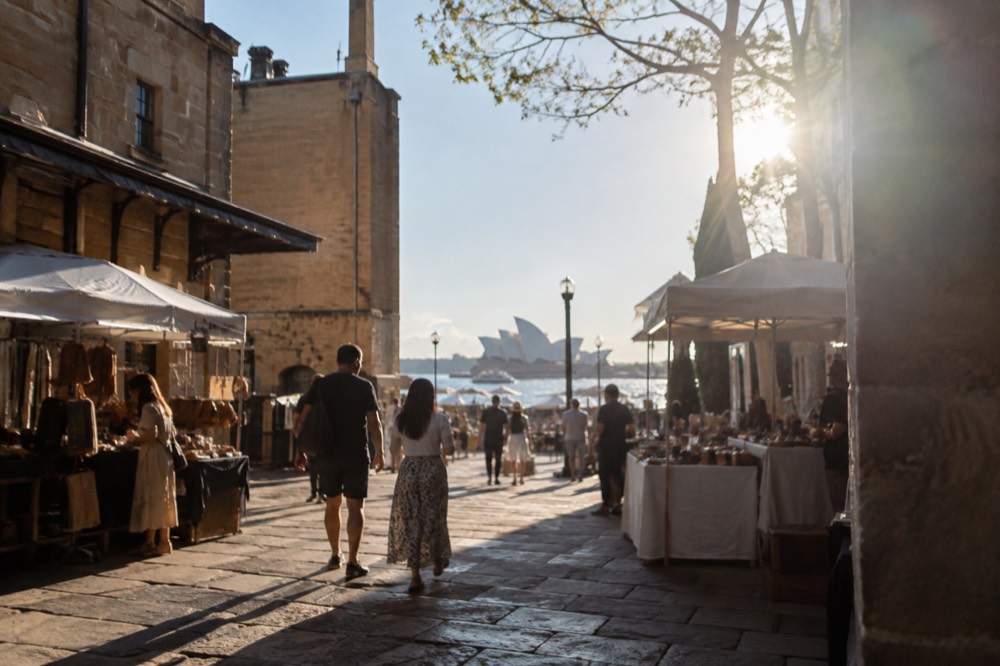 Visitors browsing market stalls under awnings in a stone-paved square in The Rocks