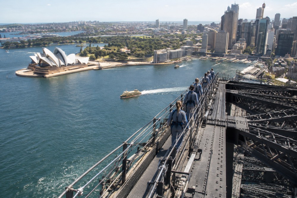The bridge arch seen from the summit plateau, with the Opera House and Circular Quay below in daylight