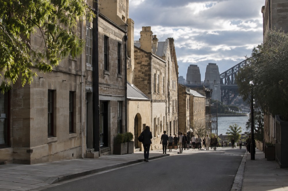The historic sandstone buildings of The Rocks beneath the southern approach of the bridge, with the check-in centre entrance on Cumberland Street