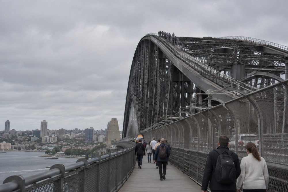 Pedestrians walking the free eastern footway across the bridge deck, with the arch and its climbing track above them