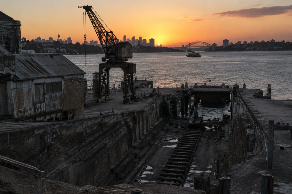 Rusted crane and old slipway structure silhouetted against a golden sunset over the harbour