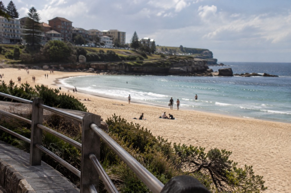 Golden sand beach curving between rocky headlands with calm water and a promenade