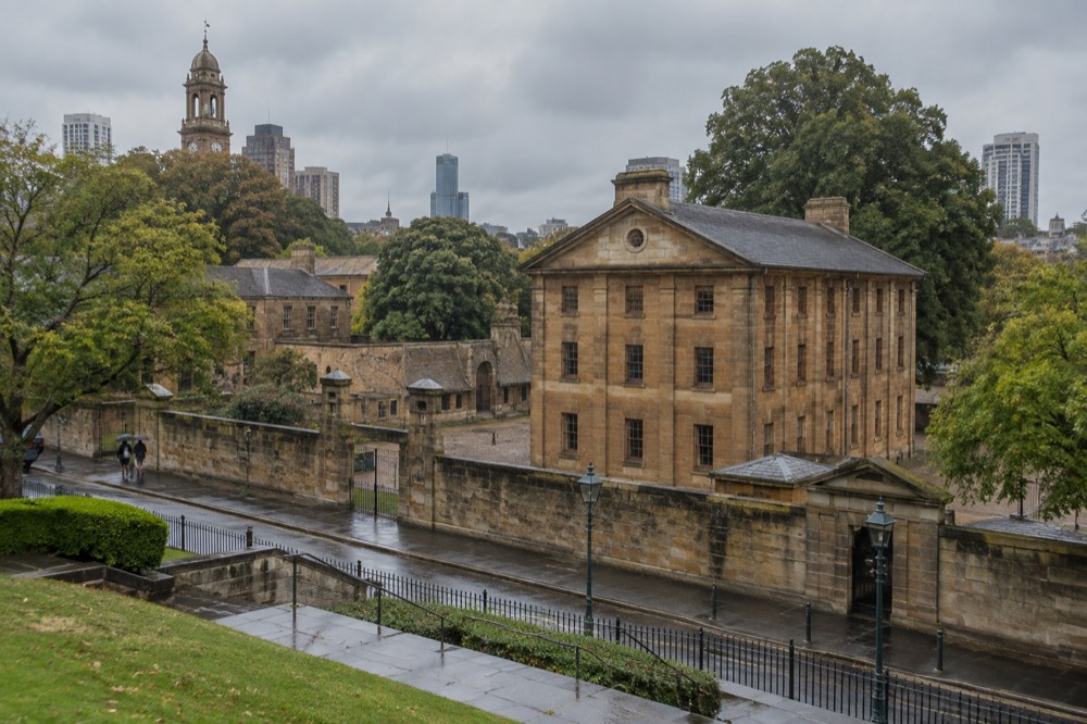 A heritage streetscape of sandstone buildings with a historic clock tower above the trees