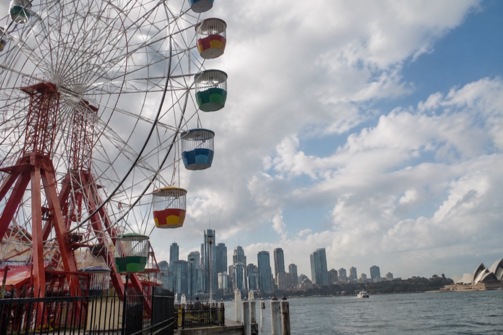 A Ferris wheel beside a harbour with a city skyline in the distance