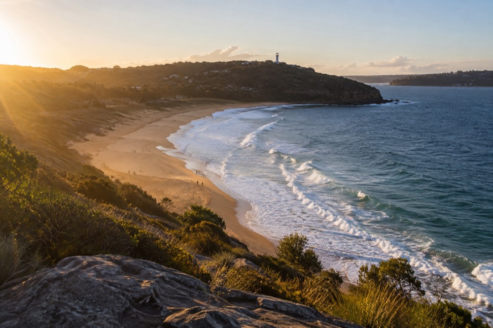 White lighthouse on a green headland above a wide sandy beach