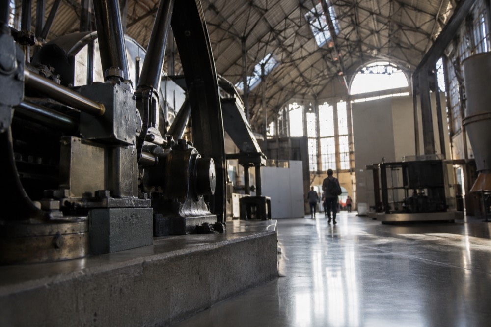 A grand heritage industrial hall with steel trusses and tall windows inside a museum building