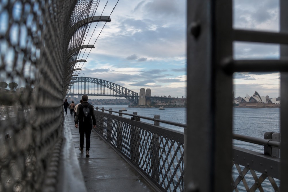 Pedestrians on the eastern walkway of the Sydney Harbour Bridge with the Opera House visible across the water