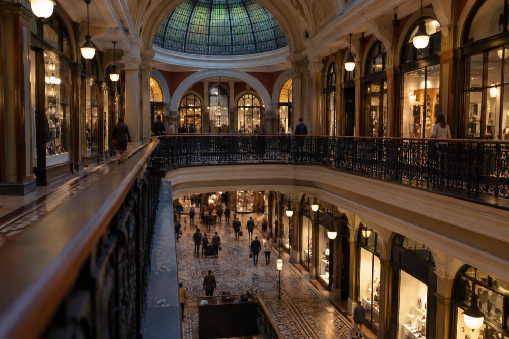 Ground-floor atrium of a heritage arcade with tiled floors, shopfronts and a domed glass ceiling overhead
